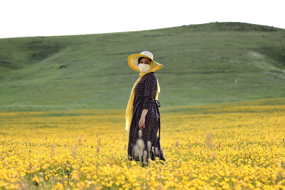 woman in black dress wearing yellow sun hat standing on yellow flower field during daytime