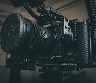 A professional camera setup featuring a Lumix camera in a SmallRig cage, equipped with a large lens and accessories. The scene is set in a dimly lit room, emphasizing the robust and high-end nature of the camera equipment.