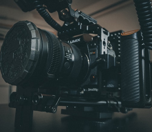 A professional camera setup featuring a Lumix camera in a SmallRig cage, equipped with a large lens and accessories. The scene is set in a dimly lit room, emphasizing the robust and high-end nature of the camera equipment.