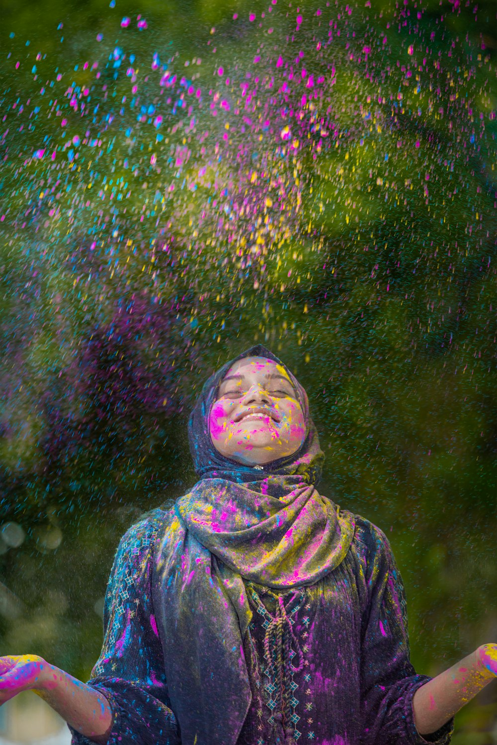 Femme en hijab vert et violet debout près de fleurs violettes