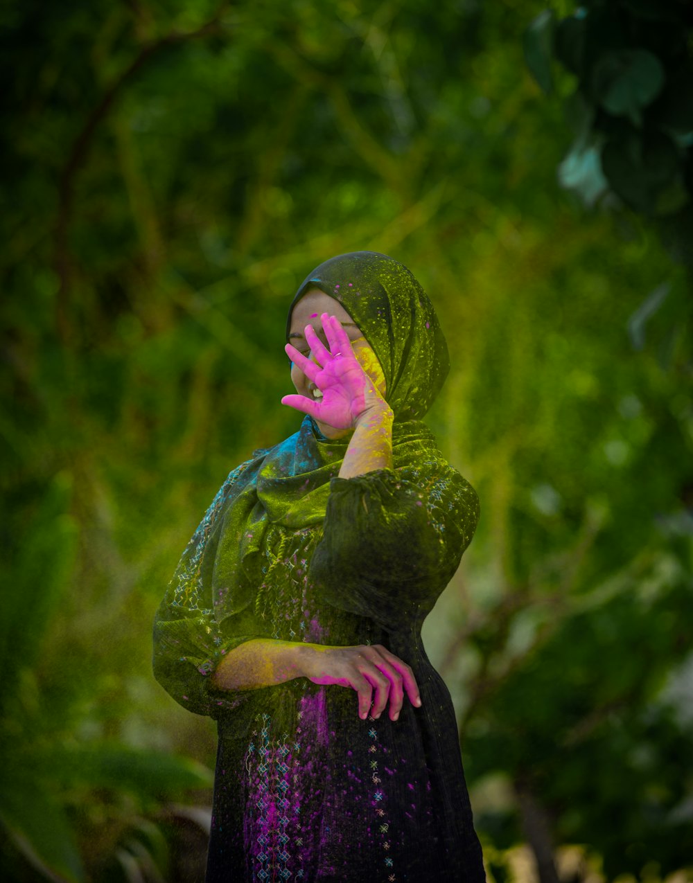 낮 동안 푸른 나무 근처에 서 있는 녹색과 보라색 꽃 드레스를 입은 여자