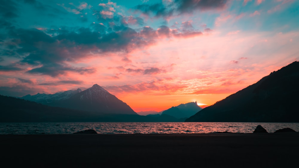 silhouette of mountain near body of water during sunset