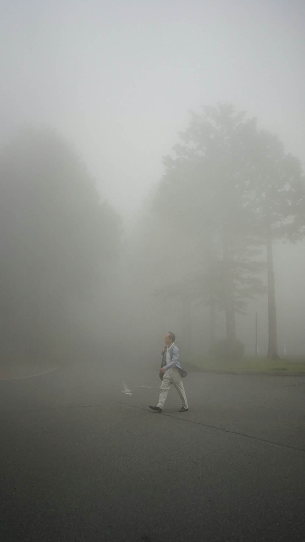 woman in white jacket and gray pants standing on gray asphalt road during foggy weather
