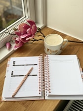 Woman journaling calmly with a light wooden desk and pale pink flowers.