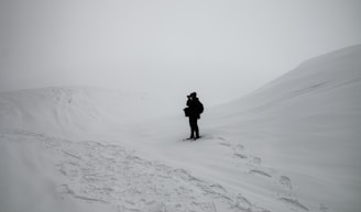 person in black jacket and pants walking on snow covered ground during daytime