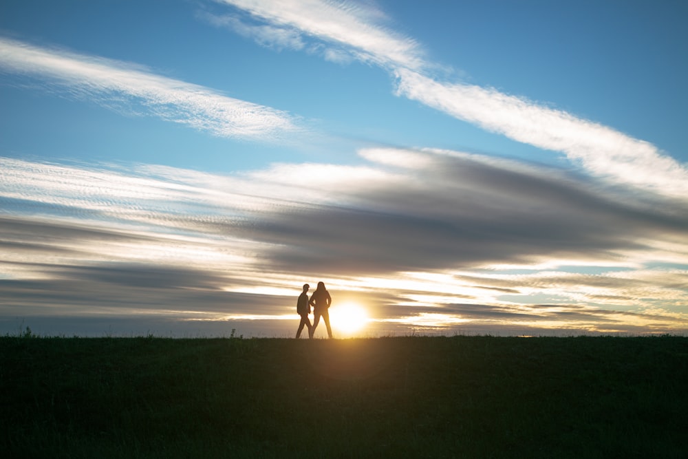 silhouette of 2 people walking on green grass field during sunset