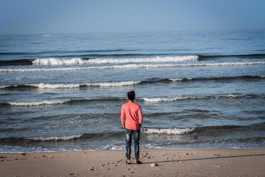 man in red hoodie standing on beach during daytime in Dwarka India