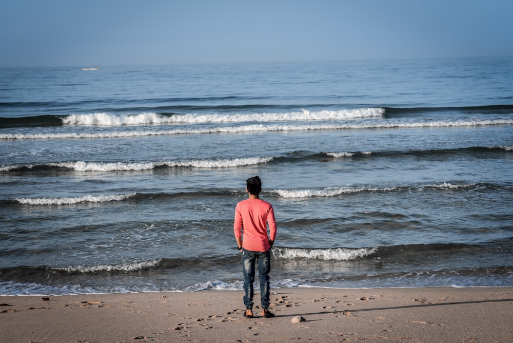 man in red hoodie standing on beach during daytime