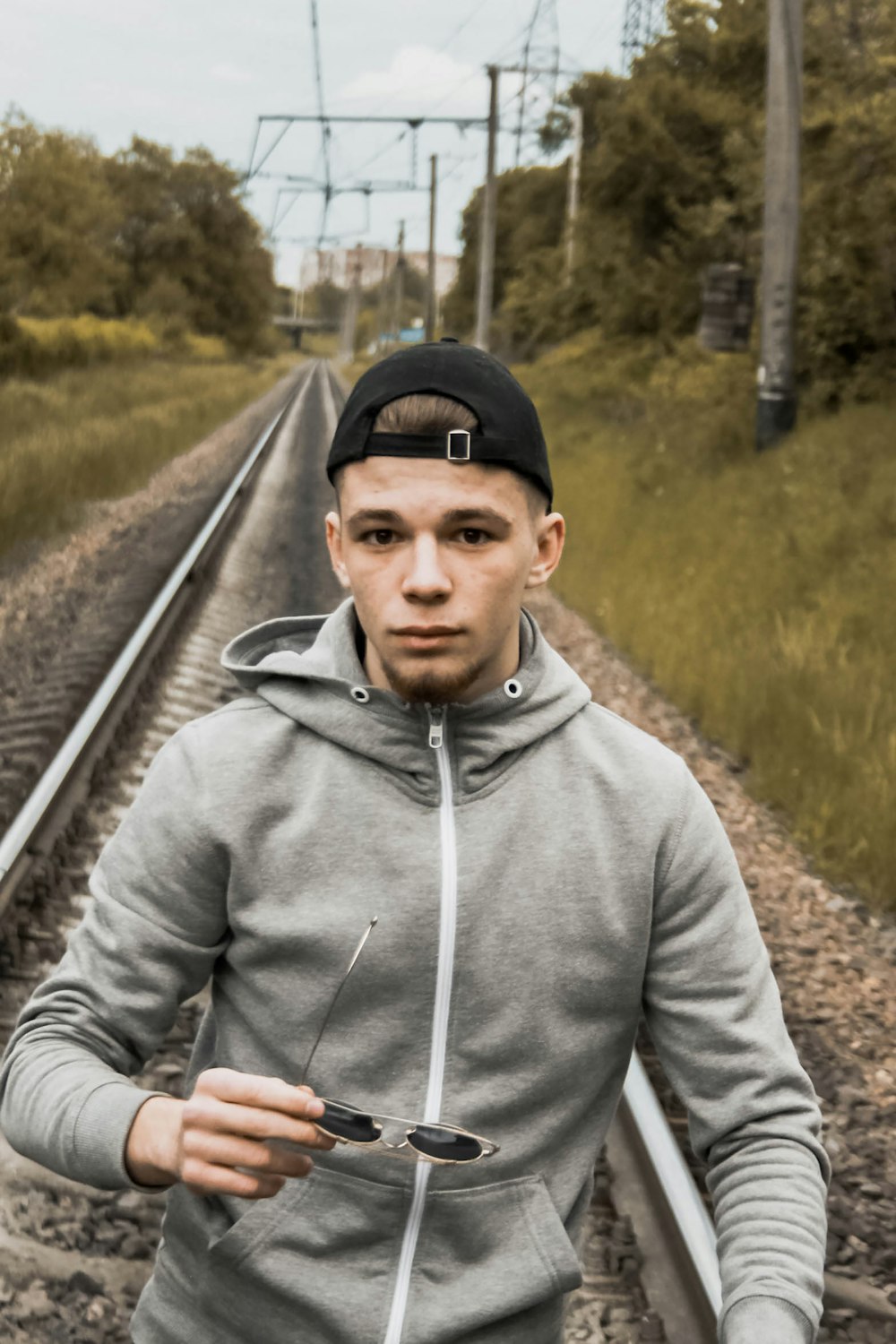 man in gray hoodie and black cap standing on train rail during daytime