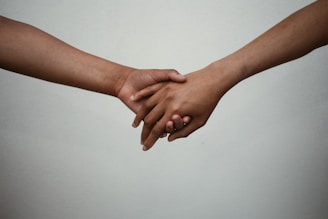 Two hands are gently holding each other against a plain background, suggesting a connection or support between the individuals.