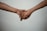 Two hands are gently holding each other against a plain background, suggesting a connection or support between the individuals.