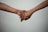 Two hands are gently holding each other against a plain background, suggesting a connection or support between the individuals.