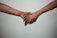 Two hands are gently holding each other against a plain background, suggesting a connection or support between the individuals.