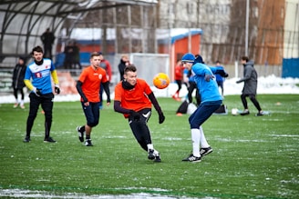 A group of diverse players enthusiastically playing pickup soccer on a grassy field, with orange and white gear.