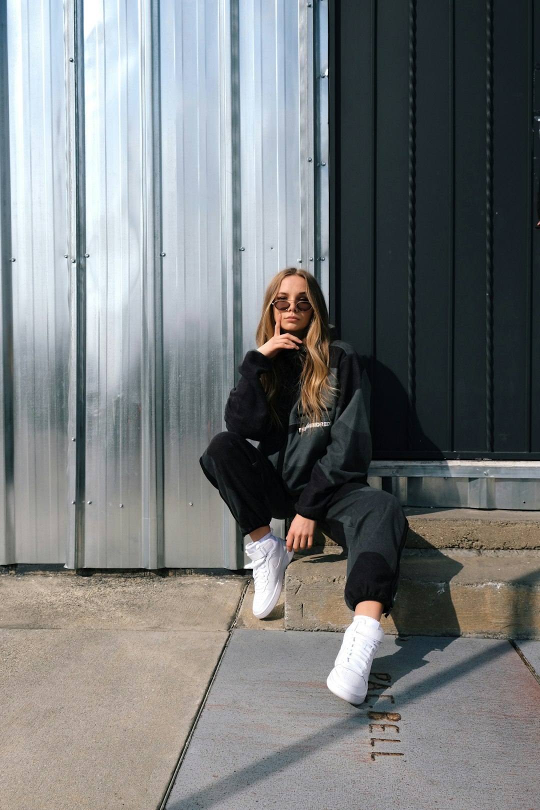 woman in black jacket and white pants sitting on gray concrete floor