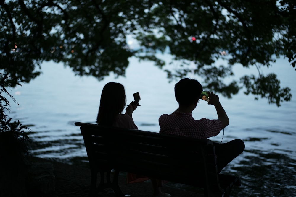 man and woman sitting on bench near body of water during daytime