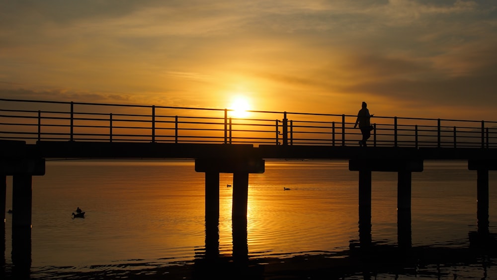 silhouette of person standing on dock during sunset