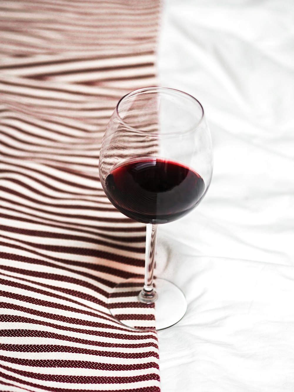clear wine glass with red wine on white and black stripe textile