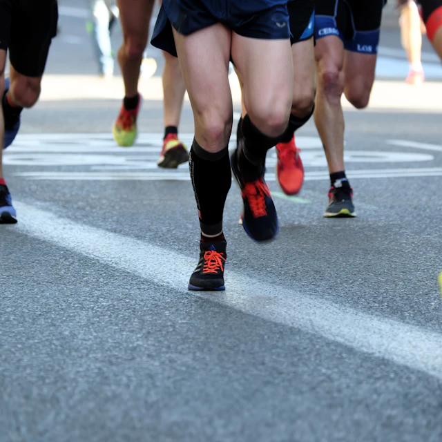 A group of people running on a grey asphalt road during the day