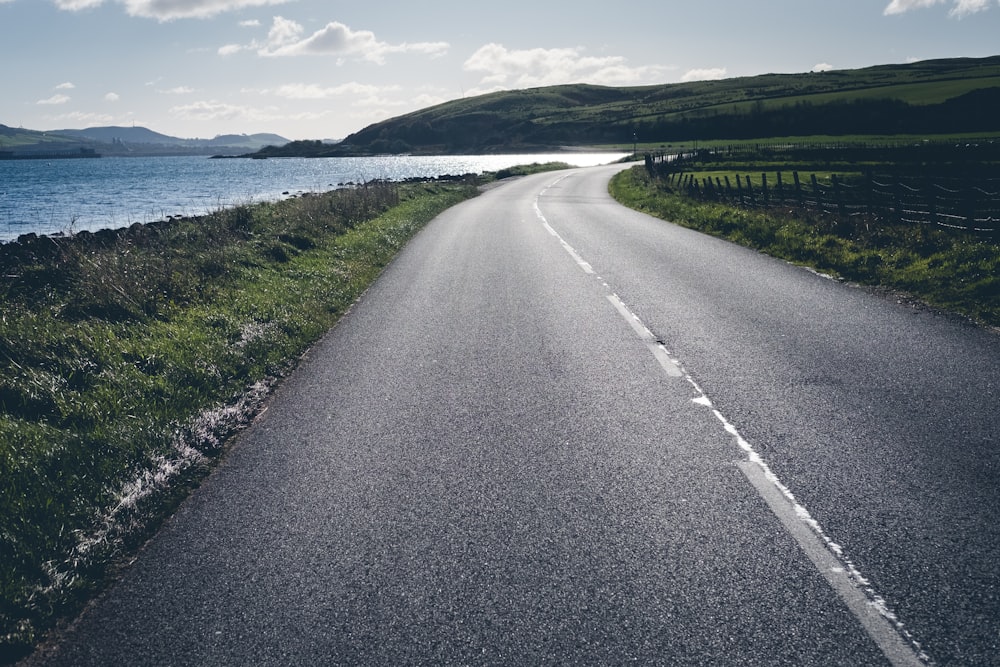 gray concrete road near green grass field and body of water during daytime