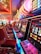 A brightly lit casino interior featuring a row of colorful slot machines. The neon lights create a vibrant atmosphere, with patterned carpeting adding to the decor. Stools are aligned neatly in front of each machine.
