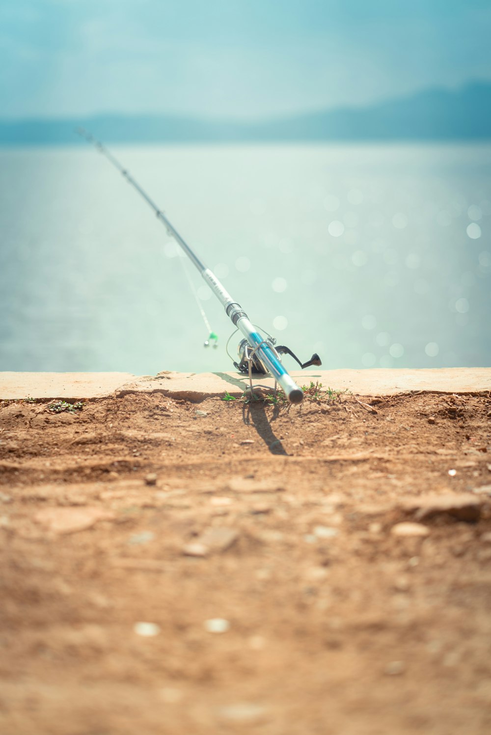 blue and silver fishing rod on brown sand near body of water during daytime