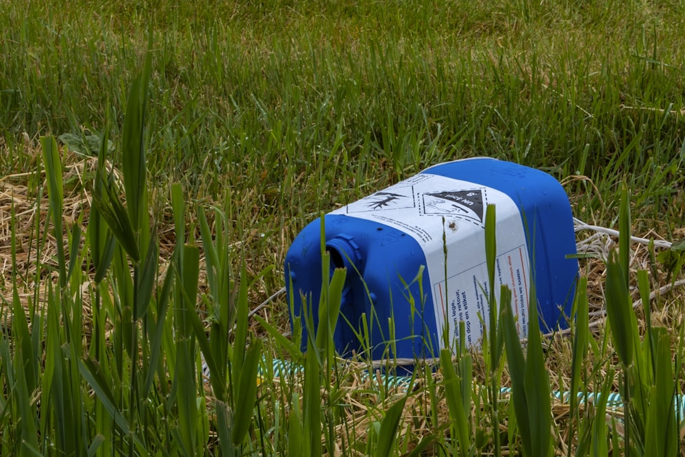 blue and white plastic trash bin on green grass field