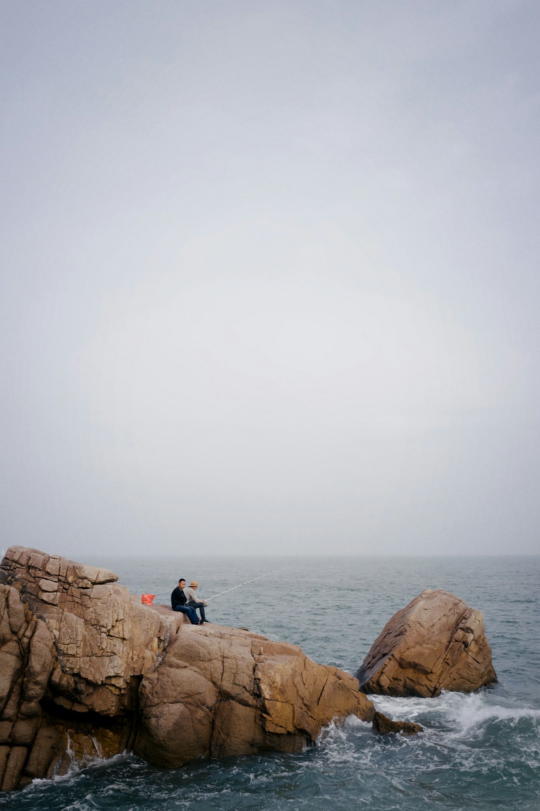 2 person sitting on brown rock formation near body of water during daytime