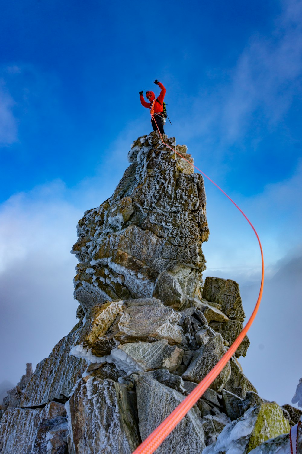 pessoa em jaqueta vermelha e calças pretas pulando na montanha rochosa sob o céu azul durante o dia