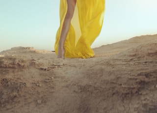 woman in yellow dress standing on brown sand during daytime