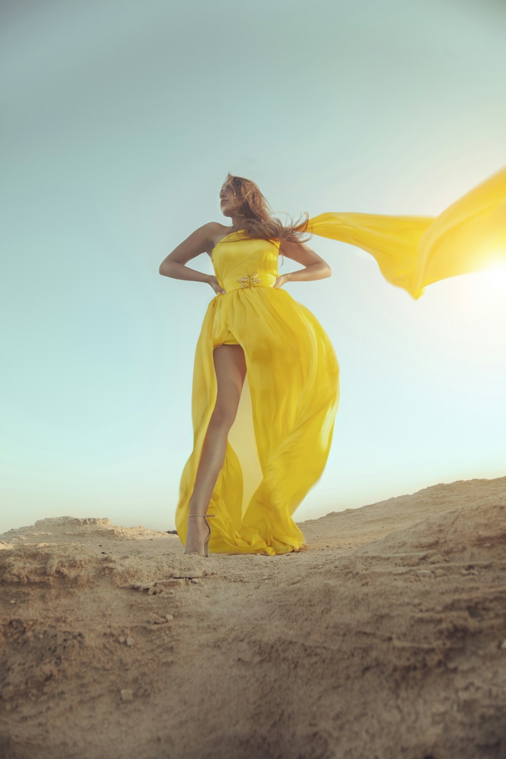 woman in yellow dress standing on brown sand during daytime