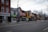 A street view featuring a row of storefronts and businesses with various signs in English and Chinese. The architecture includes brick buildings and some older, traditional designs. There is minimal activity with no visible people, and a few bicycles are parked along the sidewalk. Leafless trees line the street, and the CN Tower is visible in the background.