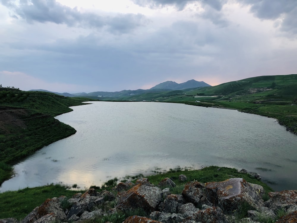 green mountain beside body of water under cloudy sky during daytime