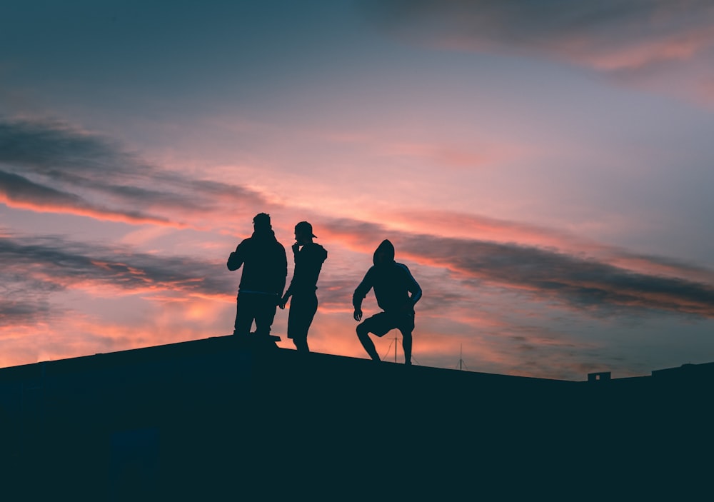 silhouette of 3 men standing on the edge of a hill during sunset