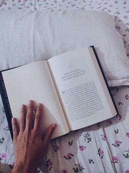 person holding book on white textile