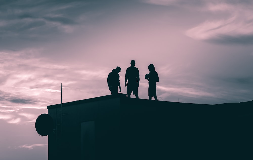 silhouette of 3 men standing on top of building during sunset