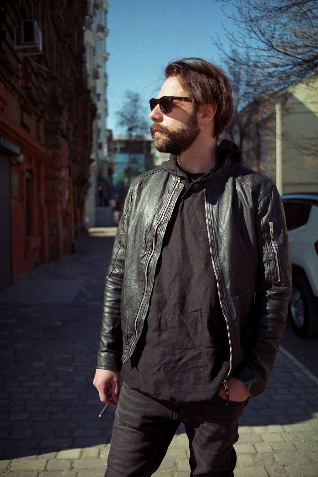 man in black leather jacket standing on sidewalk during daytime