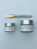 A skincare set featuring two jars and a brush. One jar is a 50ml moisturizer and the other is a 100ml clay mask, both labeled with 'YAMCO SKIN #NOFILTER'. The brush has a green handle with a gold ferrule and soft white bristles.