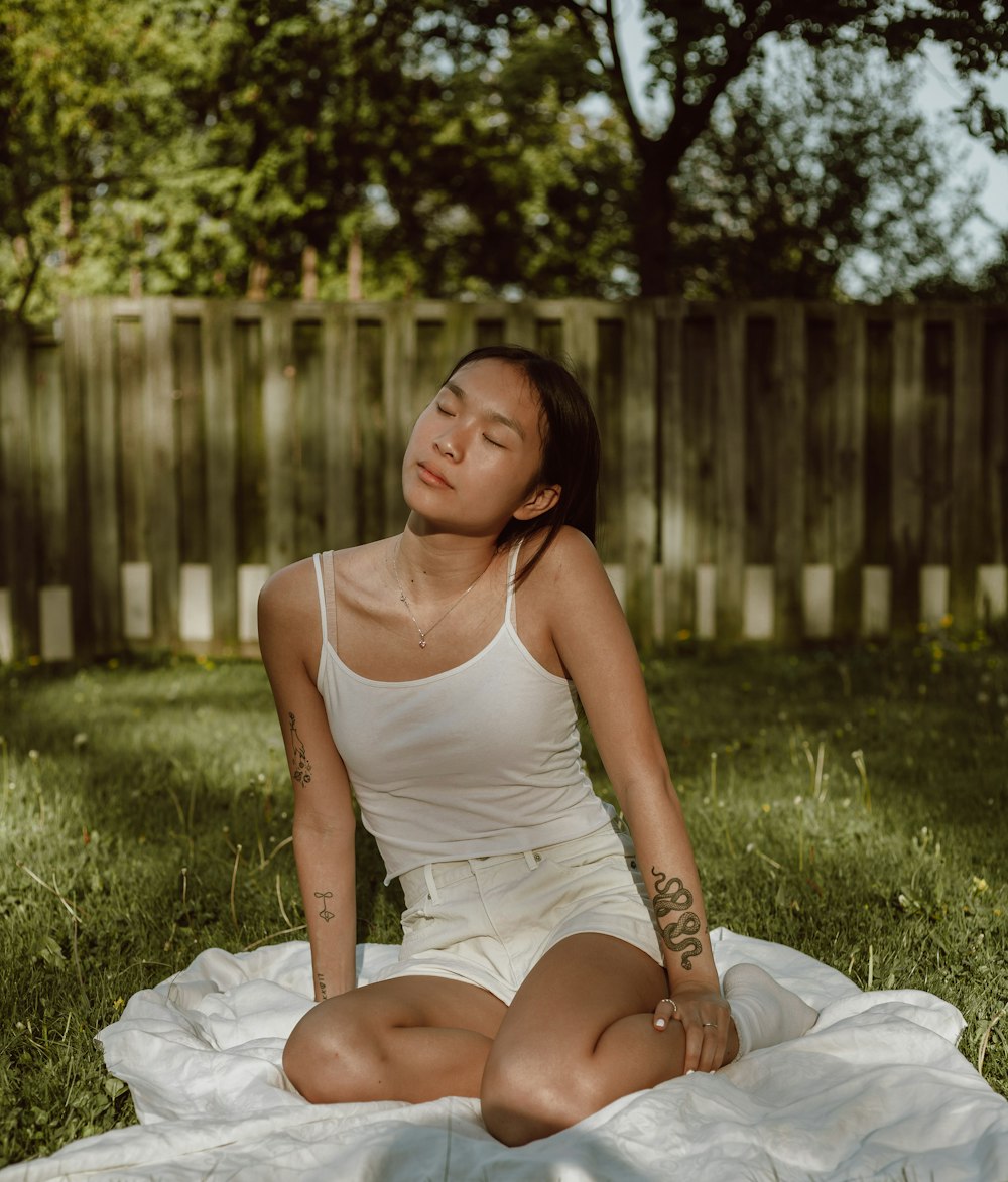 woman in white tank top sitting on green grass during daytime