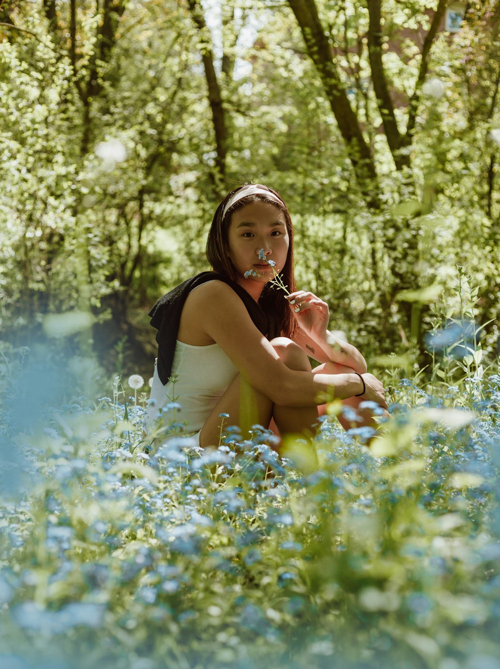 femme en débardeur noir assise sur le champ de fleurs bleues pendant la journée