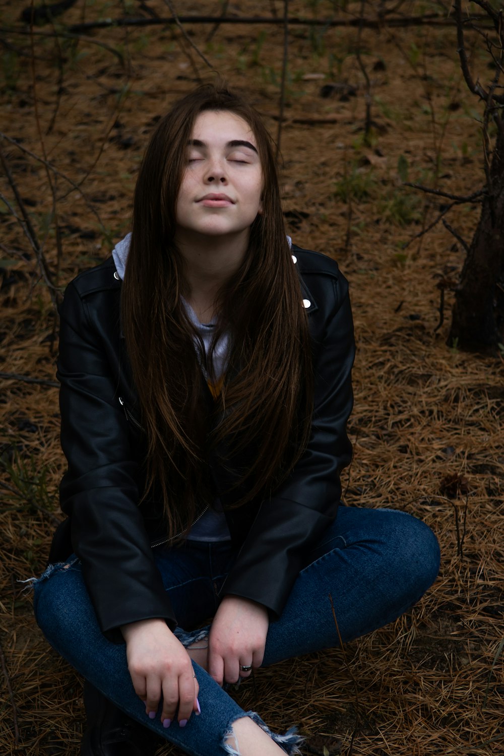 woman in black leather jacket and blue denim jeans sitting on brown grass during daytime