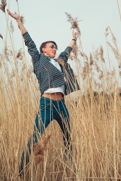 A joyful person standing with arms raised in a sunlit field, expressing confidence and faith.