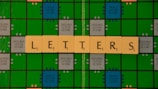 A Scrabble game board with green and blue squares is displayed, featuring beige letter tiles spelling out the word 'LETTERS' across it.