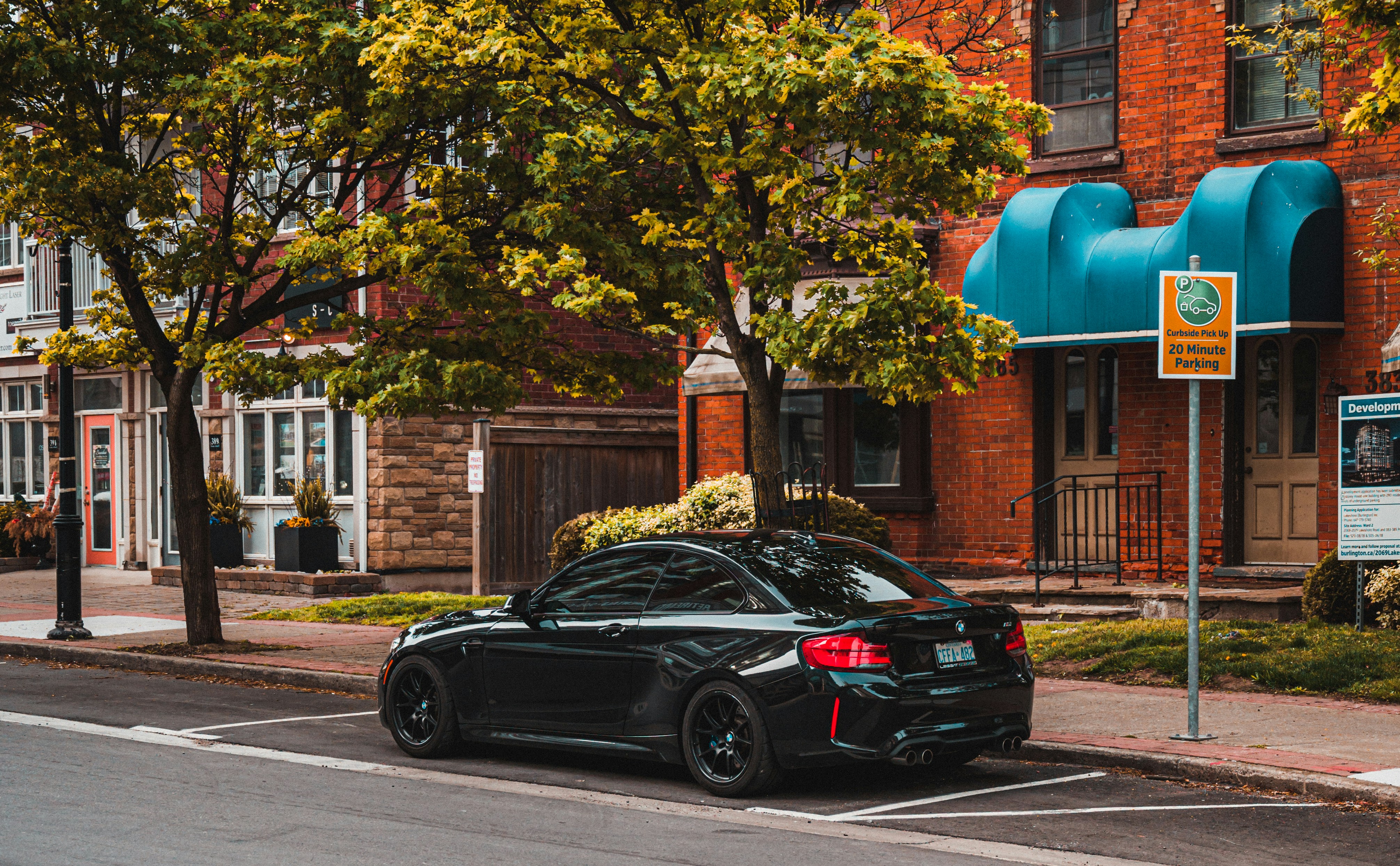 black sedan parked beside green tree during daytime