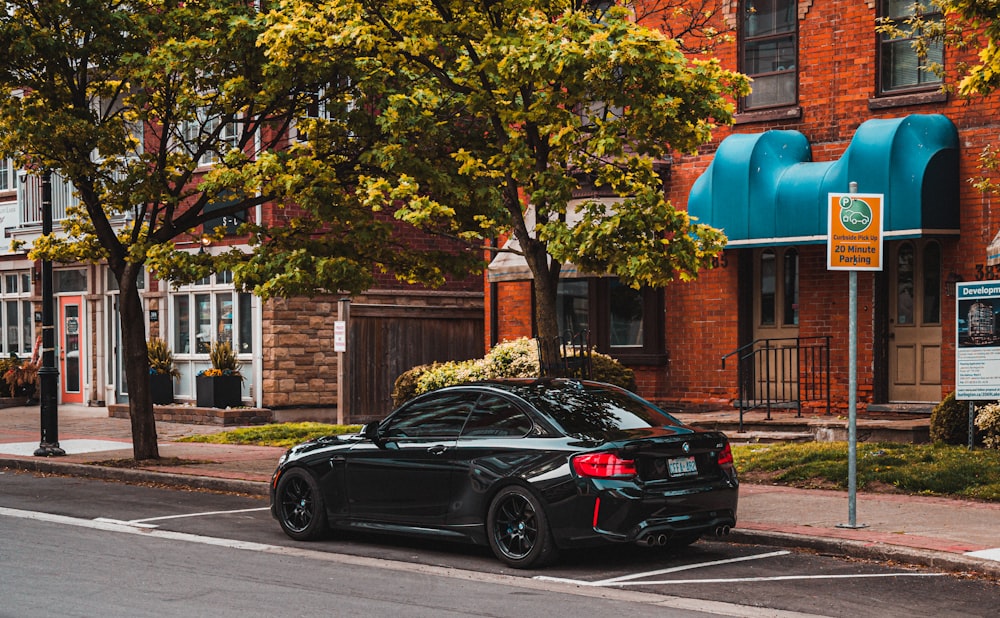 black sedan parked beside green tree during daytime