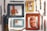 Several artistic frames are arranged on a white wooden surface, each containing a colorful caricature of a man wearing an orange shirt, with one frame displaying the image upside down. Surrounding the frames, there are various sticks and branches of different colors and shapes.