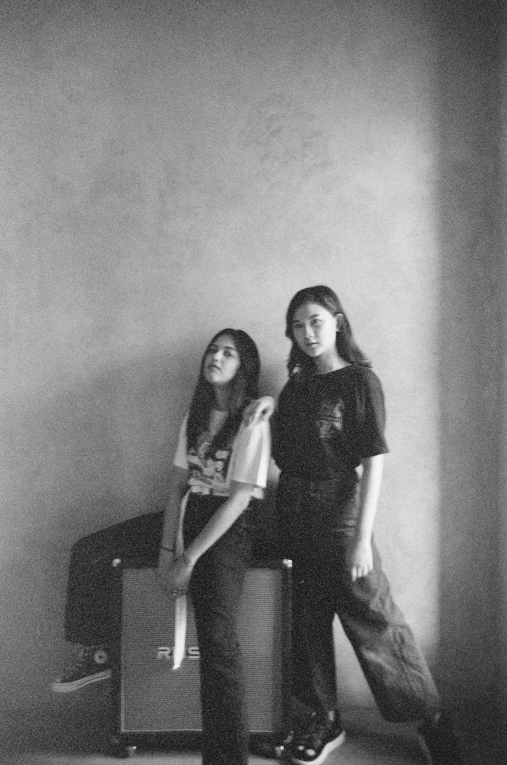 grayscale photo of 2 women standing beside wall