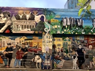 A vibrant mural depicting a diverse urban scene. The upper section features a pianist, people in formal wear, and officers with 'foreclosure' signage. The lower section shows urban life with people, pets, a classic car, police officers, and various street elements against colorful houses and buildings.