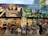 A vibrant mural depicting a diverse urban scene. The upper section features a pianist, people in formal wear, and officers with 'foreclosure' signage. The lower section shows urban life with people, pets, a classic car, police officers, and various street elements against colorful houses and buildings.