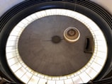 A large pendulum swings above a circular platform with marked numbers around its circumference. The setting appears to be indoors, with a focus on the pendulum's central movement and surrounding numbered markers.